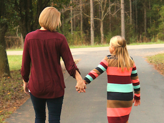An adult woman walking away holding hands with a young girl