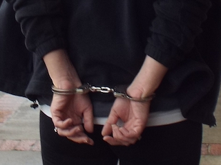 A person being led away with their hands behind them in handcuffs
