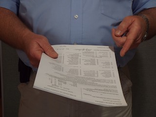 A man holding out legal paperwork in his right hand and pointing to it with his left hand