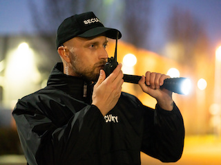 A security guard aiming a flashlight in his left hand and a radio in his right hand